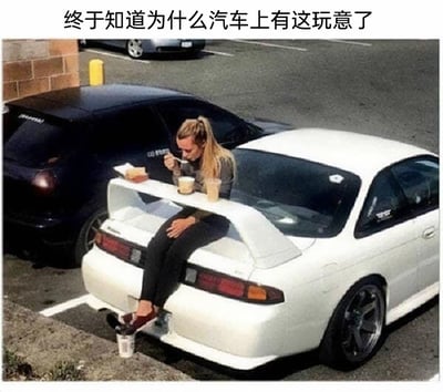 这张图片呈现了一个充满恶搞趣味的场景：一位扎马尾的女性坐在一辆白色改装轿车的大尺寸尾翼上，把原本用于优化空气动力学的尾翼当作临时餐桌，上面摆放着餐食与饮品，她正专注地用勺子进食；同时她的脚踩在一个靠汽车排气口固定的杯子上，进一步“开发”了汽车部件的另类用途。图片上方的配文“终于知道为什么汽车上有这玩意了”，用幽默的口吻调侃尾翼的功能，打破了它原本的用途设定，制造出荒诞搞笑的反差效果。