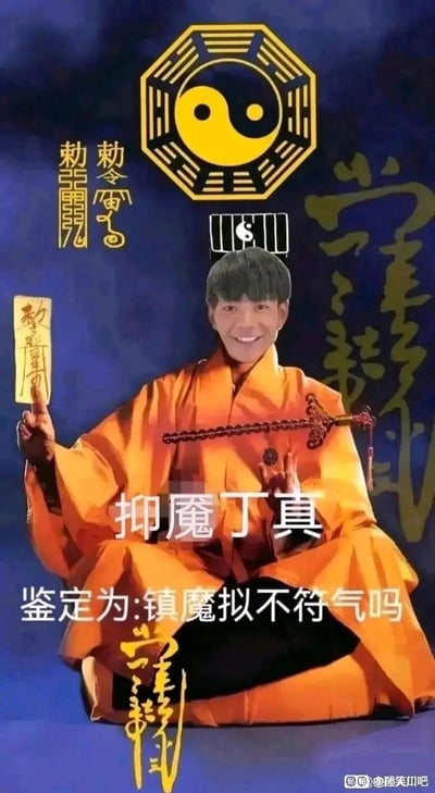 这是一张网友创作的搞笑P图，将丁真的脸部通过图像合成技术替换到身着橙色道袍、摆出打坐施法姿势的人物身体上。图中人物手持写有道教敕令的符箓，身前佩戴道教法器，背景搭配太极八卦图、道教符文和传统敕令文字。图中配有文字“抑魇丁真”“鉴定为:镇魔拟不符气吗”，运用了谐音梗：“抑魇”谐音“易燃”，“镇魔拟不符气吗”谐音反向调侃丁真相关的“针不戳（真不错）”梗，结合道教镇魔的视觉元素，整体风格戏谑搞笑，属于网络迷因类创作，用来对相关网络梗进行二次玩梗。