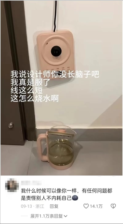 这是一张社交媒体截图，画面上方是被安装在墙面上的粉色烧水壶底座，电源线很短，下方地面上放着配套的烧水壶，两者距离很远无法对接。图中配文是发布者的吐槽：“我说设计师你没长脑子吧 我真是服了 线这么短 这怎么烧水啊”，表达了对这个不合理安装场景的不满。下方评论区有一条高赞评论，内容为“我什么时候可以像你一样，有任何问题都是责怪别人不内耗自己”，这条评论反向调侃发布者遇到问题第一时间指责他人，而未考虑是安装位置的问题，该评论获得了14.1万点赞，还有1.1万条回复。