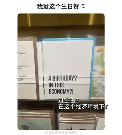 商店货架上展示着各种生日贺卡，其中一张白色贺卡格外醒目，上面用黑色大写字母写着'A BIRTHDAY? IN THIS ECONOMY?!'（过生日？在这个经济环境下？！）。图片上方配有中文文字'我爱这个生日贺卡'，下方则是英文原文的中文翻译。这张贺卡通过将生日庆祝与经济环境联系起来，形成了一种黑色幽默效果。