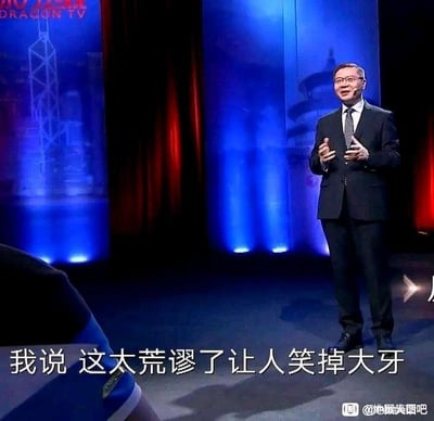 这是一张东方卫视（DRAGON TV）的节目截图，画面中一位身着深色西装、佩戴眼镜的男士站在带有红蓝灯光的舞台上，双手抬起做出演讲的手势，面部表情带着不满与嘲讽。画面底部配有白色字幕“我说 这太荒谬了让人笑掉大牙”，直白地传递出对某事的强烈吐槽情绪，这张图常被用作社交平台上吐槽离谱、荒唐事件的素材。