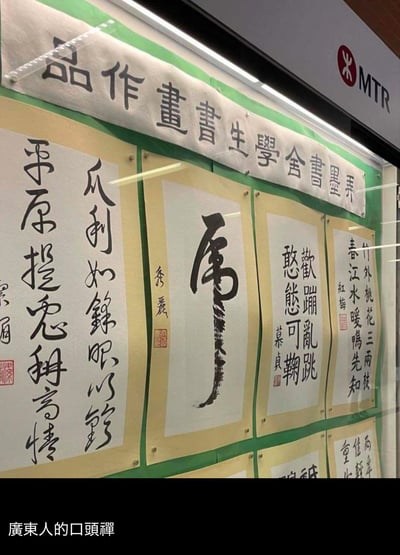 这是拍摄于香港港铁（MTR）站内的“弄墨书舍学生书画作品”展览照片，展品为多幅学生创作的书法作品，内容包含古诗、成语、单字书法等。其中一幅单字书法“属”，在粤语中与粗口“屌”谐音，搭配图片底部添加的“广东人的口头禅”文字，形成强烈的反差搞笑效果——原本正经的学生书法展览，因为这个谐音粗口梗变得滑稽有趣，调侃了粤语里的谐音文化。