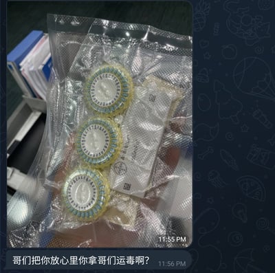 图片展示了一个透明塑料包装袋，里面装有三个圆形的蓝色和黄色药盒，以及一个白色包装。图片右下角有时间戳'11:55 PM'，底部配有文字'哥们把你放心你拿哥们运毒啊?'，时间戳为'11:56 PM'。图片有蓝色边框，上面有水果、星星等装饰图案。这是一个利用药品包装制造幽默误会的梗图，通过夸张的文字暗示这些普通药品看起来像非法物品。