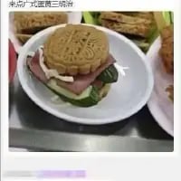 这张图呈现了一款脑洞大开的混搭食物：用广式蛋黄月饼代替西式三明治的顶部面包，搭配火腿、黄瓜、生菜等食材组合成了“月饼三明治”。图的上方配有文字“来点广式蛋黄三明治”，将传统中式月饼与西式三明治的形式结合，打造出充满反差感的创意黑暗料理，新奇的搭配让人忍俊不禁，充满趣味。