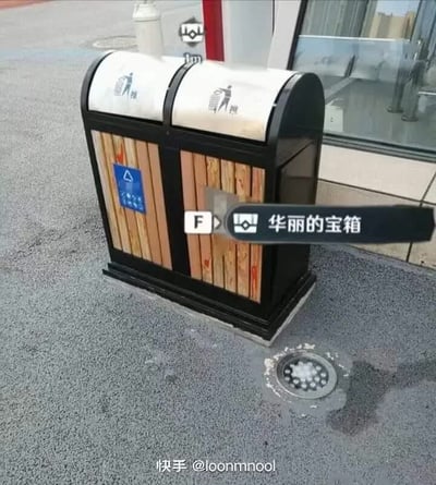 这是一张经过P图改编的趣味梗图，实拍主体是摆放在室外沥青地面上的双桶分类公共垃圾桶，背景可见建筑的玻璃门窗。创作者在垃圾桶位置叠加了开放世界游戏《原神》的专属交互提示UI，显示按下F键即可打开「华丽的宝箱」，将用来收纳垃圾的垃圾桶和游戏中能产出稀有奖励的高价值宝箱做反差绑定，制造出十足的搞笑玩梗效果，图片底部带有原发布者的快手账号水印。