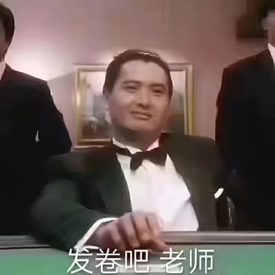 图片中是穿着黑色西装、白色衬衫和黑色领结的男子（形似周润发在《赌神》中饰演的高进），面带微笑坐在桌前，身后站着两位同样穿西装的男子。画面底部有白色文字‘发卷吧 老师’，将经典的赌神场景幽默改编为学生期待老师发试卷的场景，形成反差萌。