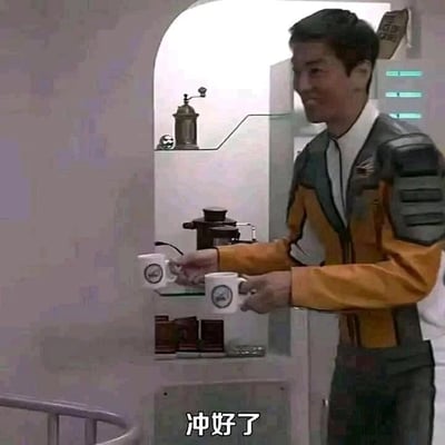 这是一张特摄剧《梦比优斯奥特曼》的影视截图，画面场景设定在GUYS防卫队的基地内部，角色相原龙身着黄灰配色的GUYS队服，脸上带着轻松的笑容，双手各端着一个印有GUYS队徽的白色杯子，正从类似茶水间的区域走出，图片下方配有字幕“冲好了”，呈现出队员在执行任务间隙的日常轻松时刻，氛围温馨。