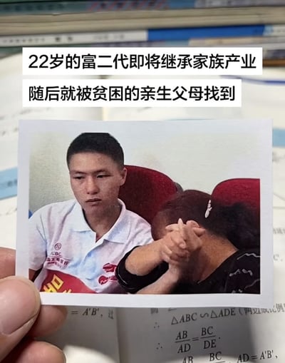 这是一张翻拍图，拍摄者用手指捏着一张新闻照片，将照片放置在印有数学公式的打开的书本上；照片上方配有两行文字说明，内容为“22岁的富二代即将继承家族产业，随后就被贫困的亲生父母找到”；照片内，22岁的年轻当事人穿着带有工商银行标识的Polo衫，坐在红色靠背椅上，神情低落沉重；他身旁坐着一位人物，是找到他的亲生父母之一，该人物双手交握抵在面部，情绪激动，挡住了自己的脸，整体内容对应配文描述的错换认亲事件。
