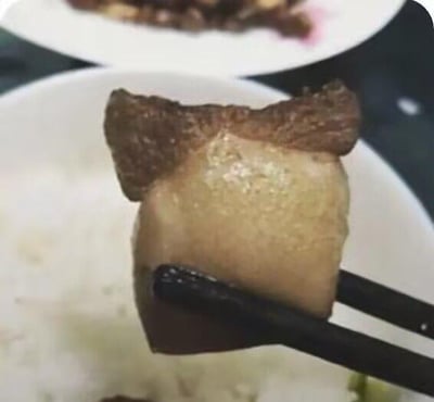 这张图中，一双黑色筷子夹起一块带皮五花肉，这块五花肉的表皮、肥瘦分层的部分恰好形成了类似人脸的轮廓，表皮的纹路像额头，肥瘦区域的分界和形态如同脸颊与面部线条，产生了有趣的视觉错位效果，让普通的食材看起来有了拟人化的模样，充满趣味，十分搞笑。