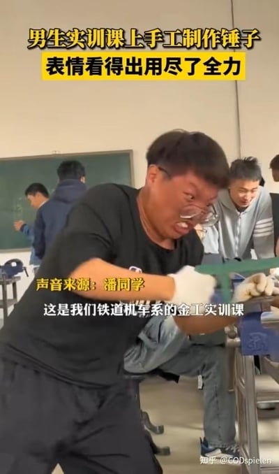 这是一张竖屏的视频截图，画面聚焦于铁道机车系的一名男生在金工实训课上的场景。该男生戴着白色劳保手套，双手紧握绿色手柄的锉刀，身体前倾，正用力锉削固定在台钳上的工件，以此手工制作锤子。他的面部表情极度夸张扭曲，眉头紧皱、眼睛眯成一条缝、嘴巴大张，看起来用尽了全身的力气。在他身后的实训教室内，其他同学有的在进行自己的实训操作，有的则坐在一旁笑着看向他，整个场景既展现了金工实训的辛苦，又充满了校园生活的搞笑氛围。画面上的文字标注清晰说明了场景背景：这是铁道机车系的金工实训课，声音来源是潘同学，还点出了男生表情用尽了全力的状态。