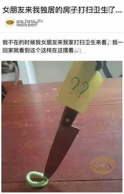图片上方是用户的文字描述：“女朋友来我独居的房子打扫卫生了... 我不在的时候我女朋友来我家打扫卫生来着，我一回家就看到这个这样在这摆着...”。下方配图中，一把刀插在木地板上，刀刃上贴着一张黄色便利贴，上面画着三个问号“???”，刀的刀尖下方有一个绿色的发圈。整体营造出一种女朋友发现不明物品（发圈）后，用刀和问号表达疑惑的幽默场景，带有情侣间常见的调侃和小紧张感。