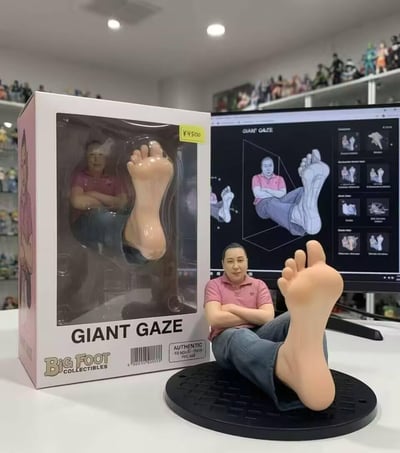 这张图展示了Big Foot Collectibles出品的「GIANT GAZE」搞怪手办：手办为一位身着粉色POLO衫、牛仔裤的人物，双臂交叉抱胸呈坐姿，一只脚被夸张放大并朝向镜头，利用视觉错位营造出「巨人凝视」的趣味效果。画面左侧是手办的包装盒，标注售价4500日元，盒身印有手办品牌与名称；背景电脑屏幕显示该手办的设计线稿图，整体场景位于摆满其他手办的收藏空间中，这款手办以荒诞的夸张设计，成为小众收藏圈的趣味藏品。