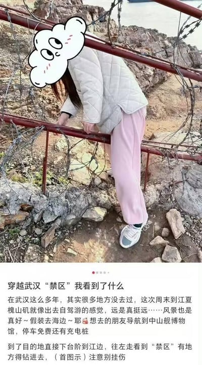 这是一篇武汉本地的小众游玩分享内容，采用图文混排的竖屏格式。上方实拍图中，一位穿着白色菱格棉服、粉色阔腿裤的女生正弯腰钻过带有铁丝网的红色栏杆，头部被一个带有害羞表情的卡通云朵贴纸遮挡，所处环境是江边的“禁区”区域，地面是碎石和泥土；下方是配套的文字攻略，分享者讲述自己在武汉生活多年，周末自驾前往江夏槐山矶，这里距离较远但风景优美，能让人有在海边的错觉，还贴心给出了导航目的地（中山舰博物馆，停车免费且有充电桩），以及到江边后钻禁区的路线提示，提醒其他游客注意别被铁丝网挂伤。