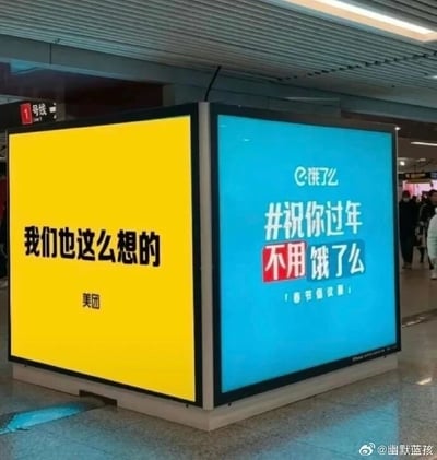 这张图片拍摄于地铁站内，展示了相邻的两个转角灯箱广告。左侧是美团的黄色背景广告，黑色字体写着“我们也这么想的”，下方标注“美团”；右侧是饿了么的蓝色背景广告，上方是饿了么的品牌标识，主体内容为“#祝你过年不用饿了么 【春节倡议篇】”，其中“不用饿了么”是双关语，既寓意着过年期间大家都能吃饱喝足不用挨饿，又巧妙嵌入自身品牌名，形成趣味的品牌表达。两个广告相邻摆放，美团的文案像是对饿了么倡议的回应，制造出品牌间有趣的联动效果，背景中可以看到地铁站的行人以及“1号线”的标识，场景真实。