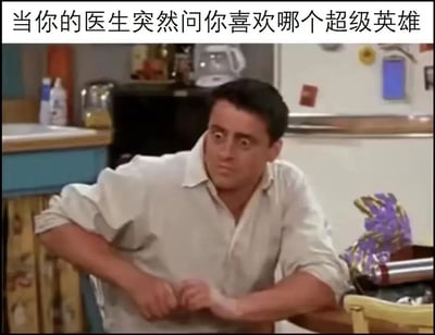 图片上方配有文字“当你的医生突然问你喜欢哪个超级英雄”，下方是一位穿着白色衬衫的男子在厨房场景中，表情困惑、眼神瞪大，身体微微前倾，似乎对这个突如其来的问题感到不解和惊讶。整体通过文字与人物表情的结合，幽默地表现出被医生问出无关医疗问题时的错愕反应。