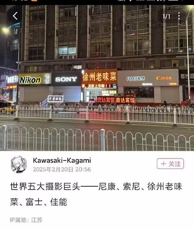 这是一张社交媒体用户发布的搞笑梗图，内容为夜晚的江苏徐州街景：街道旁的商铺依次是尼康（Nikon）、索尼（SONY）、徐州老味菜餐馆、富士（FUJIFILM）、佳能（Canon），由于餐馆恰好夹在四大摄影品牌店铺中间，用户玩梗将其与摄影品牌并列，戏称“世界五大摄影巨头——尼康、索尼、徐州老味菜、富士、佳能”，通过错位的场景制造出无厘头的幽默效果。图中还能看到街道护栏、其他小商铺以及夜晚的城市街景氛围。