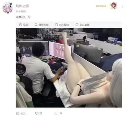这是一张微博用户发布的办公室场景截图，画面中一位男同事正专注地对着双屏电脑工作，电脑屏幕显示着二次元角色建模的内容；画面右侧的桌面边缘，一个《尼尔：机械纪元》里的寄叶二号B型（2B）角色等身抱枕，因为拍摄角度的巧合形成了视觉错位效果，看起来像是这个二次元角色的下半身正摆着抬腿姿势靠在同事的工位桌上，营造出荒诞又搞笑的画面，让普通的职场日常变得趣味十足。图中没有双关、谐音梗或暗示类内容。