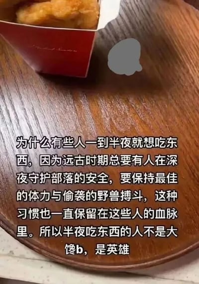 这是一张图文混排的静态图，画面上方是一份装在红色纸盒里的炸鸡，放置在深色木质托盘上，托盘区域配有一段趣味十足的文字。文字以一种幽默的“进化论”式逻辑，将半夜想吃东西的行为和远古时期守护部落、需要保持体力与野兽搏斗的英雄绑定，调侃式地为半夜嘴馋的人正名，称他们不是“大馋b”而是英雄，用荒诞又自洽的理由给深夜进食的行为赋予了有趣的英雄光环，整体风格轻松搞笑，适合用来自我调侃或者分享给有相同习惯的朋友。