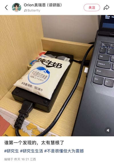 一张展示研究生生活小窍门的照片，显示一袋纯牛奶被放置在笔记本电脑充电器上加热。配文'谁第一个发现的，太有慧根了'，表达了对这种生活智慧的赞叹。