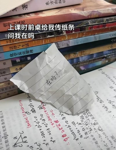 这是一张课堂场景的实拍图，画面中堆叠着多本高中教材（可见《化学反应原理》《法律与生活》等），教材下方是写满数学、化学公式与笔记的练习册，中间放置着一张皱巴巴的横线纸条，上面手写着‘在吗？’。画面上方配有文字‘上课时前桌给我传纸条问我在吗’，记录了课堂上前桌明明和自己相邻，却用传纸条的方式问‘在吗’的迷惑又搞笑的校园小瞬间，没有双关、谐音梗或暗示内容。