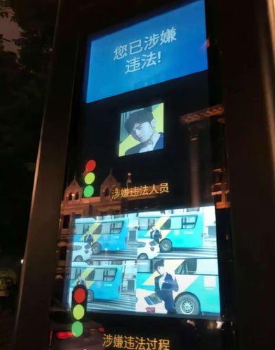这是一张网友二次创作的搞笑合成图，将周杰伦的照片放置在城市交通违法曝光设备的屏幕中，屏幕上方醒目显示“您已涉嫌违法！”，下方标注“涉嫌违法人员”，还搭配了模拟的违法过马路的画面，制造出周杰伦违反交通规则被公开曝光的反差效果，通过错位的场景结合来营造笑点，没有谐音梗或双关含义。