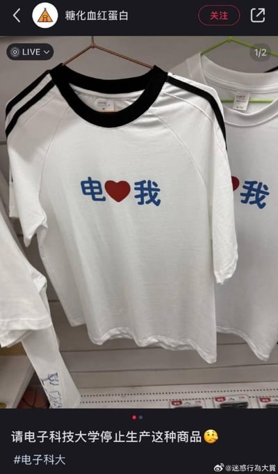 社交媒体截图显示两件白色T恤挂在衣架上，前景T恤印有蓝色“电❤️我”字样（“电”和“我”为蓝色文字，中间是红色爱心图案）。帖子配文“请电子科技大学停止生产这种商品 😂”并带有#电子科大话题标签。图中文字“电❤️我”存在谐音梗：“电”对应电子科技大学的“电子”，爱心图案替代“爱”字，形成“电爱我”的趣味表达，引发网友调侃。