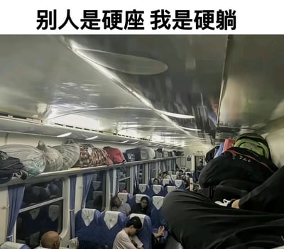 这张图片是在火车硬座车厢内拍摄的创意趣味照片，通过翻转镜头的视觉错位手法，让画面右下角的乘客腿部看起来像是躺在了车厢顶部的行李架上，营造出“硬躺”的搞笑效果。画面顶部配文“别人是硬座 我是硬躺”，与车厢内其他坐着休息的乘客形成鲜明反差，用幽默的方式调侃长途火车硬座出行的疲惫感，展现出旅途中的创意趣味。画面里可以看到蓝色的硬座座椅整齐排列，行李架上堆满了编织袋、背包等各类行李包裹，其他乘客或低头休憩或静坐，真实还原了火车硬座车厢拥挤且充满生活气息的场景。