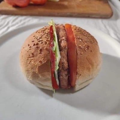 这是一张利用视觉错位技巧拍摄的创意美食照片，画面中的食物看似是被从侧面竖直切开的汉堡，能清晰看到夹在面包中的肉饼、番茄片、生菜和番茄酱，但实际上是将汉堡的上下芝麻面包片，分别放置在被切开的食材两侧，通过巧妙的摆放和精准的拍摄角度，营造出汉堡被竖切的视觉错觉，让普通的汉堡呈现出新奇有趣的视觉效果，打破了人们对汉堡常规形态的认知。