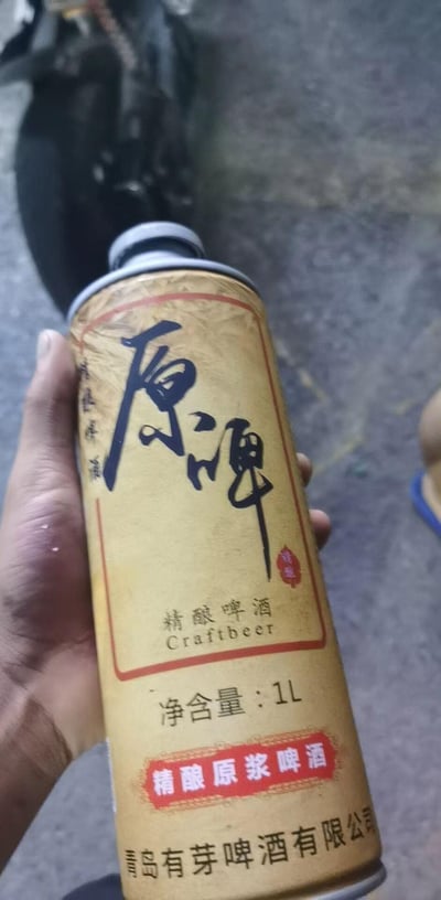 图中一只手握着一罐青岛有芽啤酒有限公司出品的精酿原浆啤酒，罐体采用复古米黄色设计，罐身印有醒目的黑色书法字体“原啤”，下方标注“精酿啤酒”“Craftbeer”“净含量：1L”“精酿原浆啤酒”等字样，整体风格偏向传统质感，是一款1升装的罐装精酿原浆啤酒。