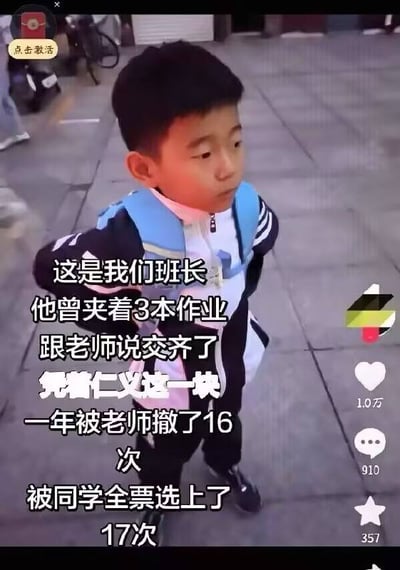 图片为社交媒体截图，显示一名穿着黑白校服、背着蓝色书包的小男孩站在户外石板路上。画面叠加文字讲述班级趣事：“这是我们班长 他曾夹着3本作业 跟老师说交齐了 凭着仁义这一块 一年被老师撤了16次 被同学全票选上了17次”，展现了班长在老师与同学间的反差形象，充满幽默校园气息。右侧有社交媒体互动数据：1.0万点赞、910评论、357收藏，左上角有“点击激活”按钮。