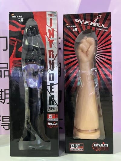 图片展示了两个IGNITE品牌的成人情趣玩具产品包装盒，左右并排摆放。左侧包装盒为黑色和红色设计，印有'THE INTRUDER ARM'字样，内含一个黑色手臂造型的玩具，包装上标注'15" PLUS SUCTION'和'PHTHALATE FREE'。右侧包装盒为红色和黑色放射状图案设计，印有'THE REBEL EXTREME'字样，内含一个肉色拳头造型的玩具，包装上标注'12.5" PLUS SUCTION'和'PHTHALATE FREE'。两个包装盒顶部均有IGNITE品牌标识。