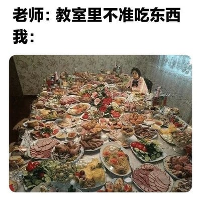 图片上方配有文字“老师：教室里不准吃东西 我：”，下方是一张实拍照片：一张巨大的餐桌上摆满了琳琅满目的食物，包括各种肉类、蔬菜、点心等，一名穿着粉色衣服的人坐在餐桌旁。通过老师禁止在教室吃东西的规则与“我”摆出满桌盛宴的夸张行为形成强烈反差，制造出幽默搞笑的效果。