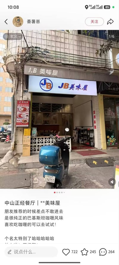 社交媒体截图展示了用户“番薯崽”分享的中山餐厅“JB美味屋”实拍场景。照片中可见餐厅临街门面，招牌“JB美味屋”字样醒目，门口停放一辆蓝色电动车，店内隐约可见桌椅陈设。配文称这是朋友推荐的巴基斯坦咖喱餐厅，因店名“特别”差点不敢进入，实际口味纯正，推荐给咖喱爱好者。图中幽默点源于店名缩写引发的联想，带来轻松调侃的效果。