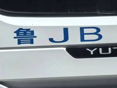 一张汽车尾部的特写照片，展示了车牌的部分内容。照片中可以清晰看到蓝色的“鲁JB”字样，其中“鲁”是中国山东省的车牌简称。在车牌下方，有一个部分可见的汽车品牌标识，显示为“YUT”。图片聚焦于车辆的牌照区域，背景为白色车身。