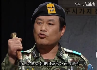 这是一张来自B站的视频截图，画面中是一位身着韩国迷彩军装、头戴贝雷帽的中年男性演员，他手持类似指挥刀的物件，嘴巴微张，正处于发言状态，画面下方配有白色字幕“历史定然会对我们做出公正的评价”，背景上方还有韩文标识，整体场景是在演绎一段正式的、与历史评价相关的发言内容。