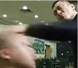 图片展示了一个室内冲突场景，一名男子正挥拳猛烈击打另一名男子的头部，被打者因冲击力头部向后仰，画面动感强烈，氛围紧张激烈。场景可能发生在餐厅或类似公共室内空间，背景可见模糊的灯光和陈设。