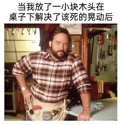 这是一张经过二次创作的搞笑梗图，图上方配有中文文字“当我放了一小块木头在桌子下解决了该死的晃动后”，图中主体是一位穿着格子衬衫、系着装满工具的腰带，看起来专业感十足的男性工匠，他一手叉腰，一手扶在桌面上，脸上带着得意自信的神情。这张图的笑点在于，角色的专业工匠身份和配文里用小块木头垫桌子这种敷衍却实用的“治标不治本”解决方案形成强烈反差，用幽默的方式调侃生活中这种简单粗暴却有效的小技巧，让观众产生共鸣。