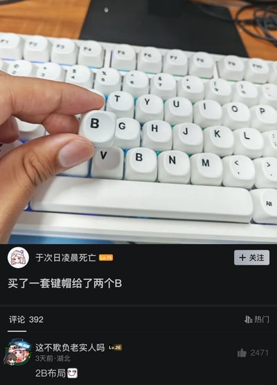 这是一张社交媒体截图，上半部分实拍了白色机械键盘，一只手的拇指和食指捏着一个额外的印有字母B的键帽，而键盘原本的B键位置已经安装了一个B键帽，整套键帽一共得到了两个B；下半部分展示社交平台帖子内容，发帖用户“于次日凌晨死亡”配文“买了一套键帽给了两个B”，下方热评用户玩梗评论“2B布局😉”，整体契合标题“two b or not two b”，谐音莎士比亚名句“To be or not to be”，同时双关两个B键帽和网络用语“2B”的含义，形成趣味梗图效果。