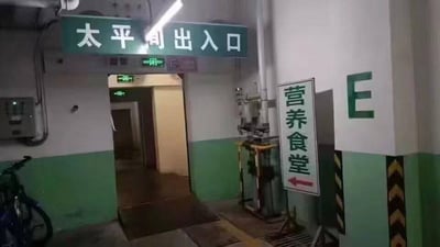 这是一张医院内部的实拍照片，画面上方悬挂着绿底白字的「太平间出入口」标识，下方是通往太平间的通道；通道右侧立有一个指向左侧的「营养食堂」指示牌，食堂的方向与太平间出入口完全一致。这种极具违和感的场景布局，很容易让看到的人产生荒诞、不适的联想，引发关于医院场景设置合理性的讨论。