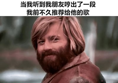 图片上方配有文字'当我听到我朋友哼出了一段我前不久推荐给他的歌'，下方是一位金发络腮胡男性的侧脸特写。他穿着棕色外套，背景模糊，眼神略带笑意望向一侧，表情中透露出满足和一丝不易察觉的得意，生动展现了推荐的音乐被朋友接受并记住时的欣慰心情。