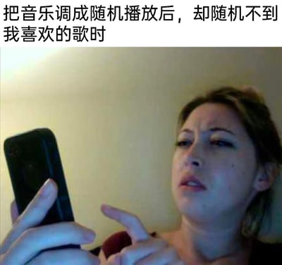 这是一张文字加注的真人表情包，上方配文“把音乐调成随机播放后，却随机不到我喜欢的歌时”，图中的女性眉头紧皱，眼神带着不满与疑惑，嘴巴微张，一只手拿着手机，另一只手指向手机，表情烦躁又疑惑，精准还原了人们在使用音乐软件随机播放功能时，反复刷不到自己想听的歌曲，产生无奈、烦躁情绪的日常场景，容易引发大众共鸣，常被用于社交平台表达这类小情绪。