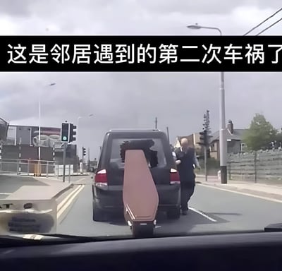 图片显示一起交通事故现场，从车辆内部视角拍摄。一辆黑色汽车停在道路中间，车尾伸出一个大型红色物体，疑似家具或设备。一名男子站在车旁，似乎正在处理事故。背景中可以看到城市街道、交通信号灯和建筑物。图片上方有文字说明："这是邻居遇到的第二次车祸了"。