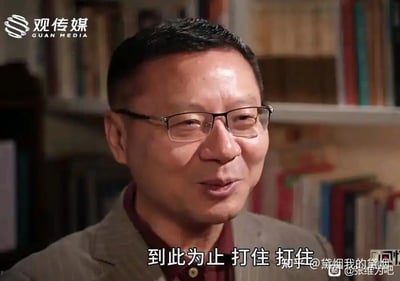 这是一张源自采访视频的梗图，图中人物为学者张维为，他戴着眼镜，面露略带笑意的无奈表情，嘴巴微张，似乎正在打断对话。画面底部配有字幕「到此为止 打住 打住」，这个截图被网友制作成表情包，常用于聊天场景中表达想要终止某个话题、不想继续讨论的情绪，直白地传递出叫停的态度。
