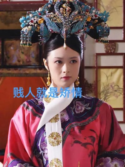 图片为电视剧《甄嬛传》中角色华妃的剧照截图，华妃头戴装饰有蓝色凤凰、珍珠和宝石的华丽凤冠，身着红色为主、紫色镶边并绣有花卉图案的宫装，背景为古色古香的木质窗框和屏风。图片中央叠加蓝色文字“贱人就是矫情”，这是华妃的经典台词，原用于讽刺甄嬛装模作样，现常被网民用于戏谑调侃虚伪做作的行为。