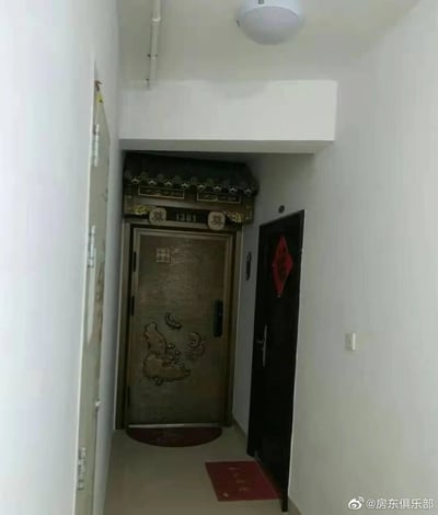 这张照片拍摄于居民楼的狭长楼道中，画面尽头是1301号住户的家门，该住户将门楣装修成带有中式传统屋檐的样式，门楣两侧还设置了写有“奠”字的装饰，使得家门整体外观类似灵堂布置，门体本身带有鱼形浮雕；在其右侧的邻居家门上贴着红色的福字，与1301号门的风格形成强烈的视觉反差。楼道墙面为白色，顶部安装有吸顶灯，整体场景展现出一种令人不适的视觉冲突，属于邻里间的特殊装修事件。