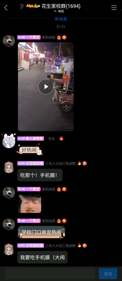这是一张竖屏的手机聊天群截图，群名为“花生家校群(1694)”，时间显示为21:31。群内成员围绕用户“一个秀才”分享的学校门口夜晚热闹夜市的视频展开互动：“一个秀才”配文“茉莉绿茶 🔥🥰”分享视频后，又发送搞怪人脸表情包和“学校门口肯定热闹”的带图消息；用户“毛毛”回复“好热闹”；用户“小艾拉の犬”玩梗，先后说“吃那个！手机膜！”“我要吃手机膜（大闹”，将夜市里的手机贴膜摊位玩成“吃手机膜”的趣味梗，整体群聊氛围轻松诙谐，是普通社群成员的日常趣味互动。