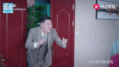 图片中是网络热梗“龙王赘婿”的经典场景，演员管云鹏穿着灰色西装，推开红色双开门，面带标志性的“歪嘴一笑”，双手张开作迎接或宣告状。背景可见室内环境，整体画面充满戏剧性。该场景源自2020年爆红的免费网文推广广告，体现了“卑微赘婿-身份揭露-打脸逆袭”的爽文模式核心瞬间。