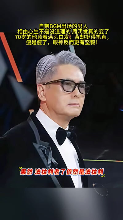整张图的主体是70岁的周润发，他留着银白头发，佩戴黑框眼镜，身着黑色西装礼服搭配领结，腰背挺直，表情沉稳坚毅，气质出众。图上方配文介绍70岁的周润发虽身形清瘦但精神状态极佳，图下方配文“果然 法拉利老了依然是法拉利”，用热梗夸赞周润发历经岁月仍保有极佳的个人魅力与状态。