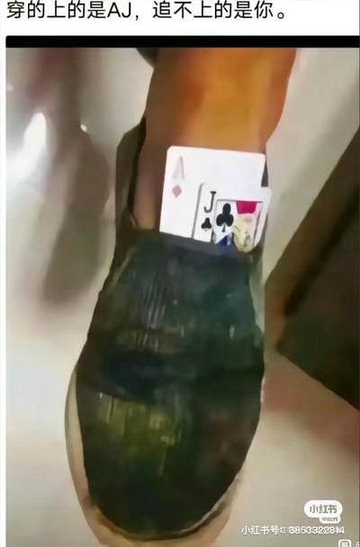一张创意梗图，展示了一只穿着绿色鞋子的脚，脚踝处夹着一张A牌和一张J牌，巧妙组合成"AJ"。图片上方配有文字"穿的上的是AJ，追不上的是你。"，通过双关语制造幽默效果 - 表面指能穿上AJ鞋(用扑克牌A和J代表)，深层含义则是表达追不到心仪对象的无奈。