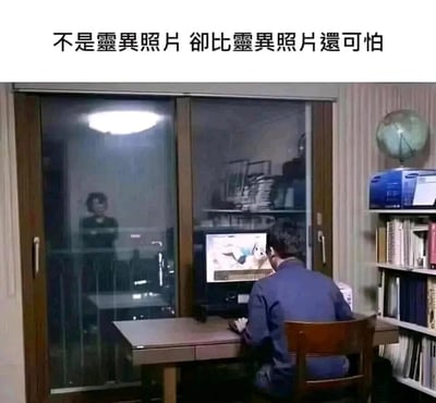 这是一张记录家庭日常社死场景的静态图。画面中，一名男性背对着镜头坐在书桌前，正专注地看着电脑屏幕上的二次元风格内容；在他身后的玻璃推拉门外，一名女性正严肃地注视着他，玻璃的反光效果让这个场景乍一看类似灵异画面，但实际上是真实的生活场景。图片上方配有文字“不是灵异照片 却比灵异照片还可怕”，精准点出了年轻人在私下爱好被长辈突然撞见时，那种比灵异画面更让人恐慌、尴尬的社死感受，很容易在ACG爱好者群体中引发共鸣。